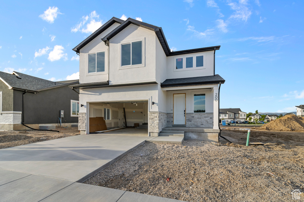 View of front of property with a garage, stone siding, concrete driveway, and stucco siding