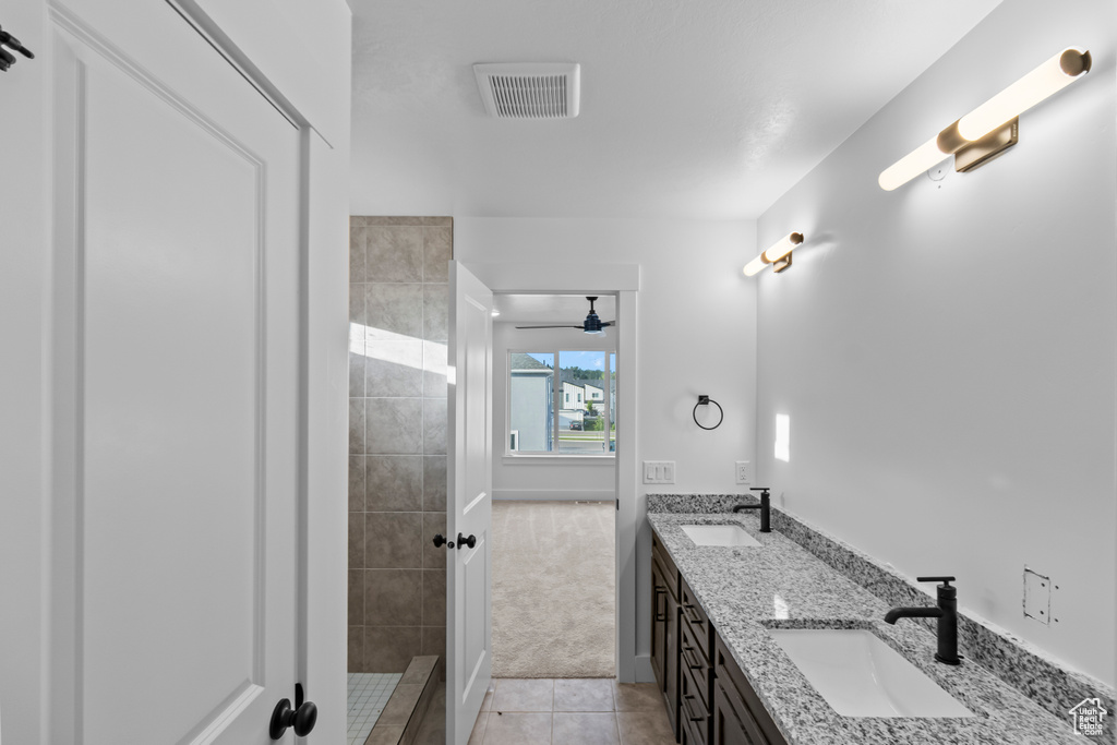 Bathroom with double vanity, tile patterned flooring, tiled shower, and baseboards