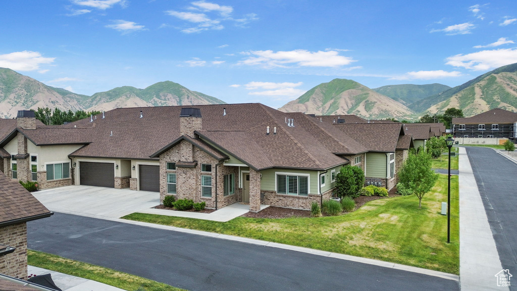View of front of house with brick siding, a mountain view, an attached garage, driveway, and a front lawn