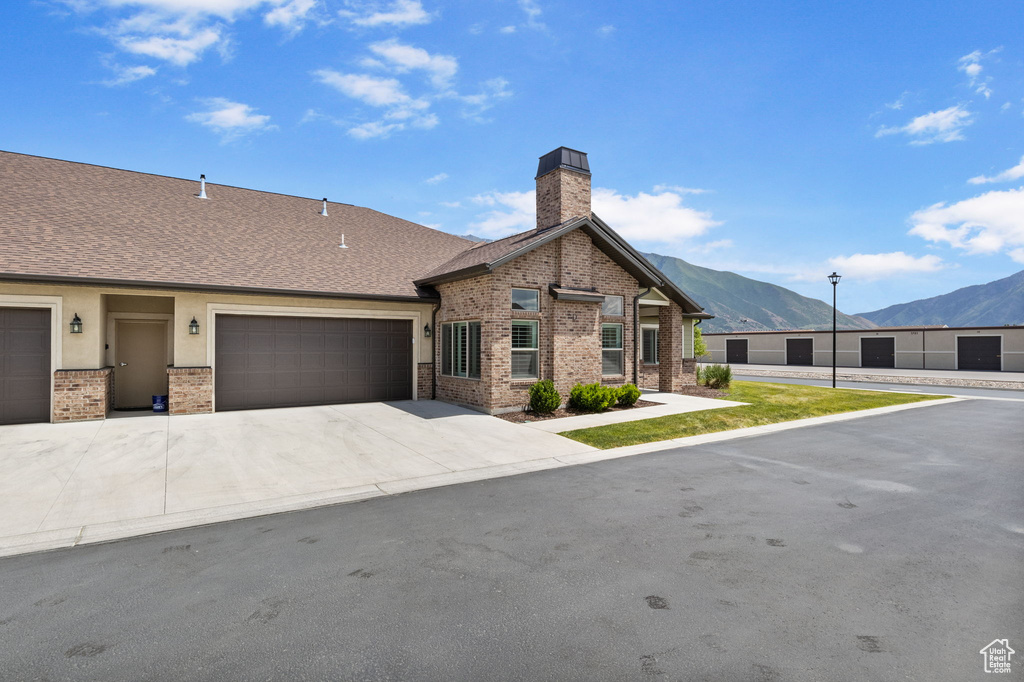 View of front facade with a mountain view, a chimney, brick siding, concrete driveway, and a garage