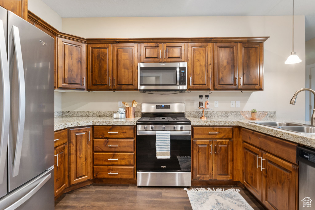 Kitchen featuring appliances with stainless steel finishes, dark wood finished floors, a sink, pendant lighting, and light stone counters