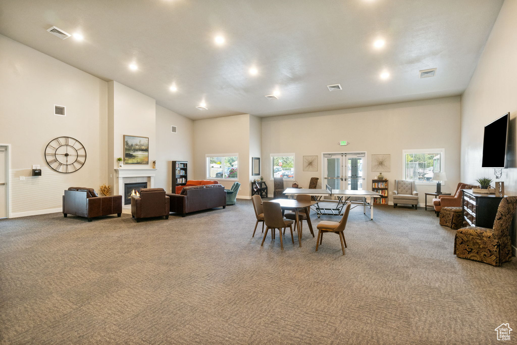 Dining area with a towering ceiling, light colored carpet, french doors, a warm lit fireplace, and baseboards