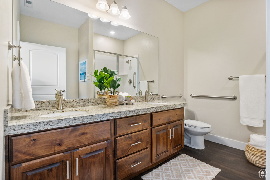 Bathroom featuring baseboards, double vanity, wood finished floors, a shower stall, and toilet
