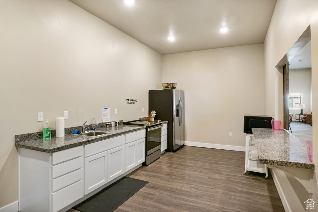 Kitchen featuring appliances with stainless steel finishes, a sink, dark wood finished floors, white cabinets, and baseboards