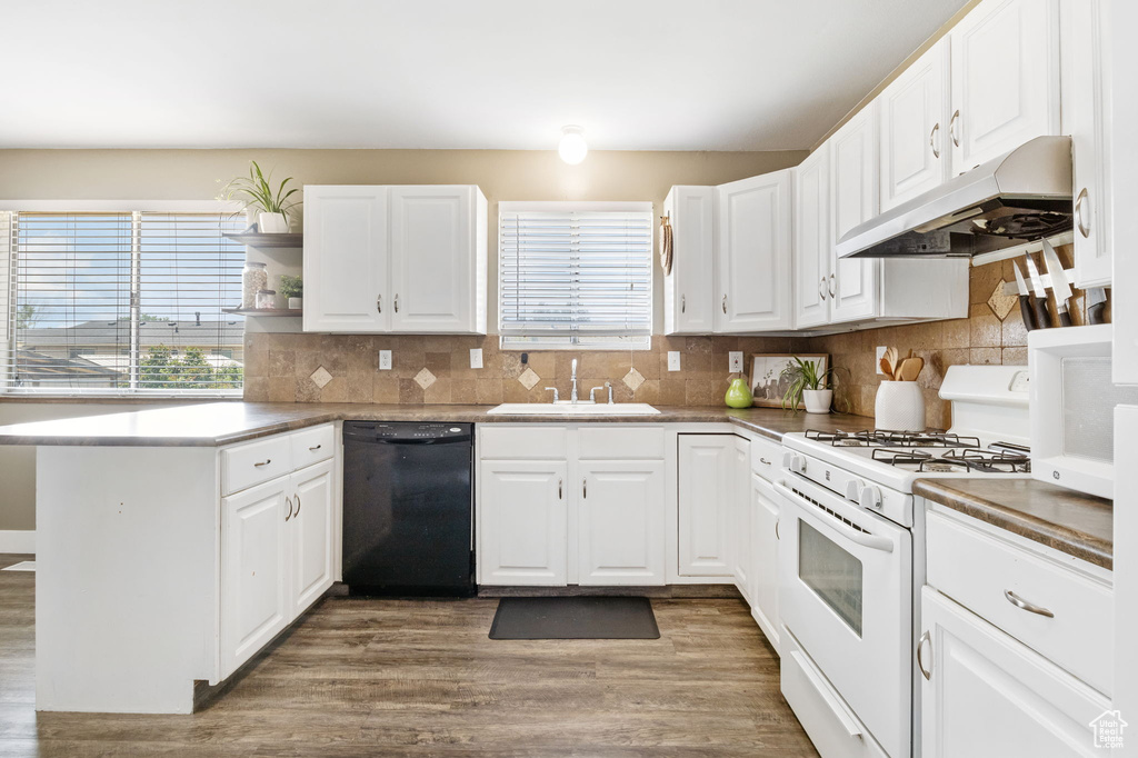 Kitchen featuring black dishwasher, white gas range oven, a sink, under cabinet range hood, and wood finished floors
