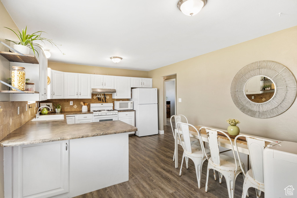Kitchen featuring white appliances, under cabinet range hood, a sink, a peninsula, and decorative backsplash