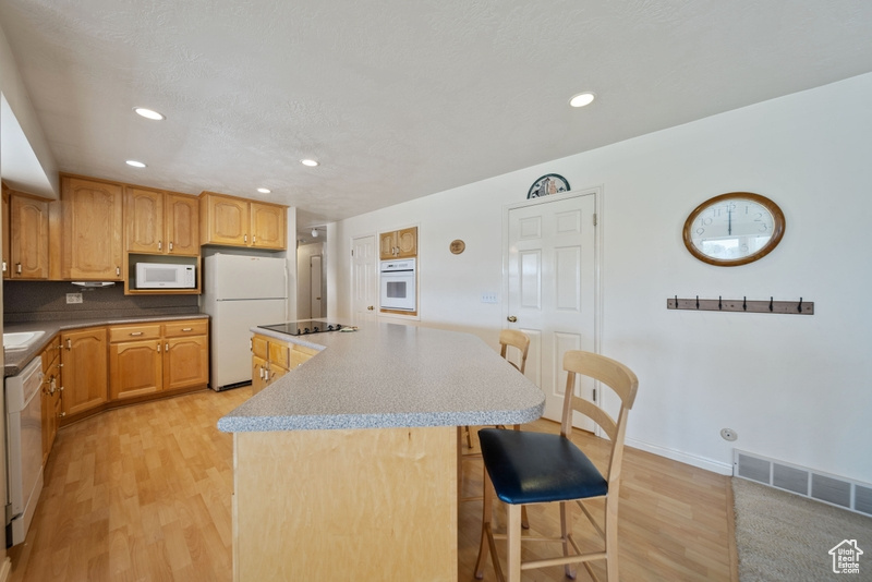 Kitchen featuring white appliances, a center island, light wood-type flooring, a breakfast bar area, and recessed lighting