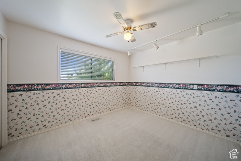 Carpeted empty room featuring a ceiling fan, rail lighting, and wainscoting