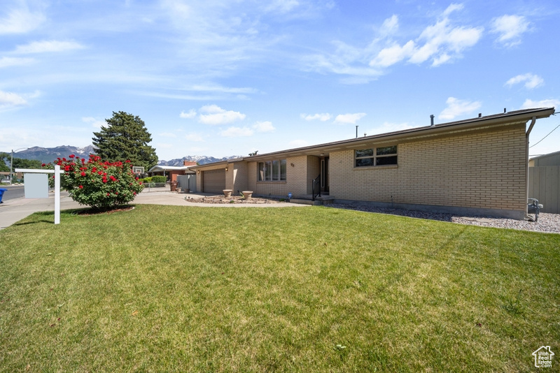 Back of property featuring a garage, brick siding, driveway, a yard, and a mountain view