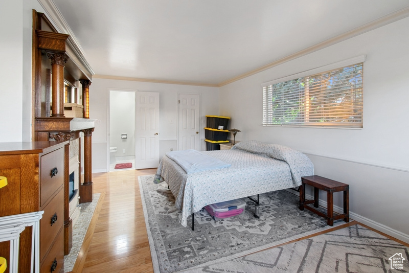 Bedroom with light wood finished floors, ornamental molding, and ensuite bathroom