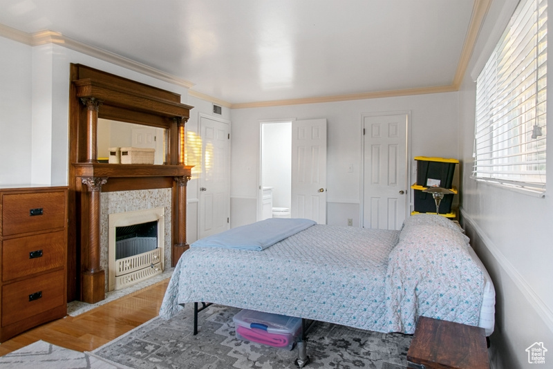 Bedroom with wood finished floors, crown molding, and a fireplace