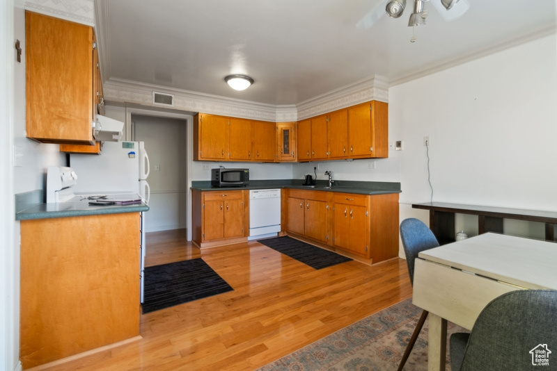 Kitchen with white dishwasher, stainless steel microwave, brown cabinetry, ventilation hood, and light wood-type flooring
