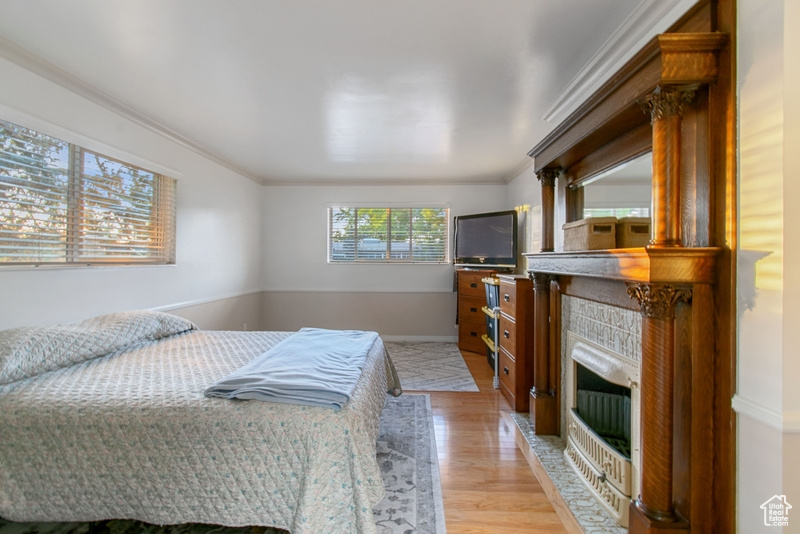 Bedroom featuring light wood-type flooring, ornamental molding, and a fireplace