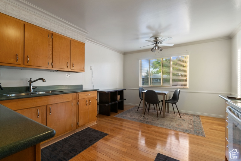 Kitchen with a ceiling fan, crown molding, light wood finished floors, dark countertops, and brown cabinets