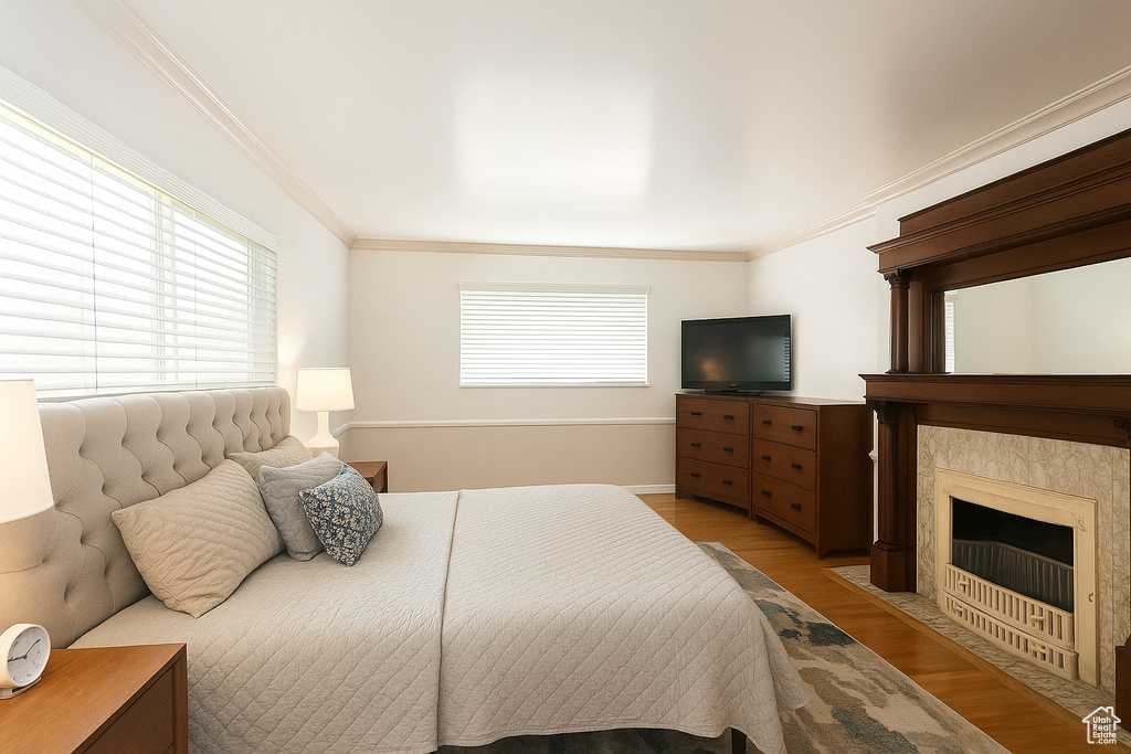 Bedroom with light wood finished floors, crown molding, a premium fireplace, and baseboards