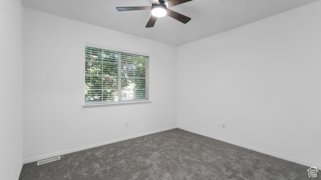 Spare room featuring a ceiling fan, dark colored carpet, and baseboards