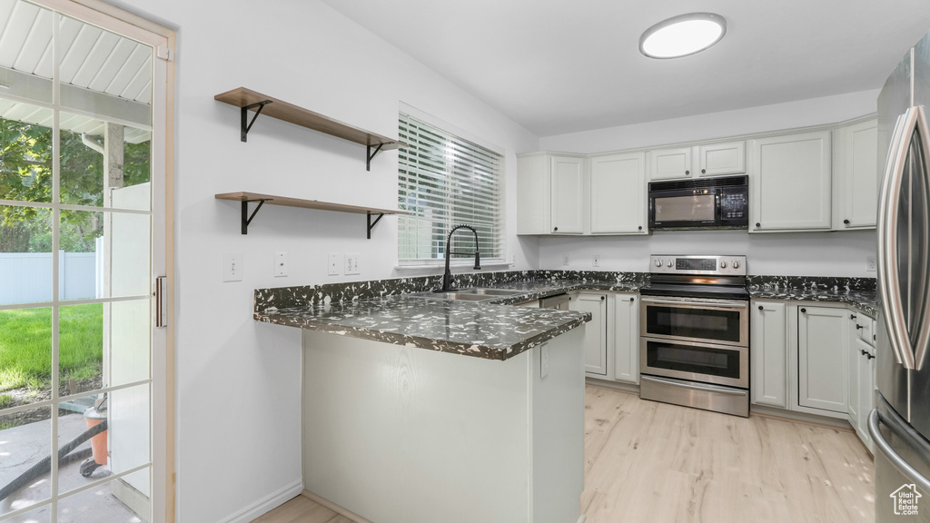 Kitchen with stainless steel appliances, a sink, dark stone countertops, and healthy amount of natural light