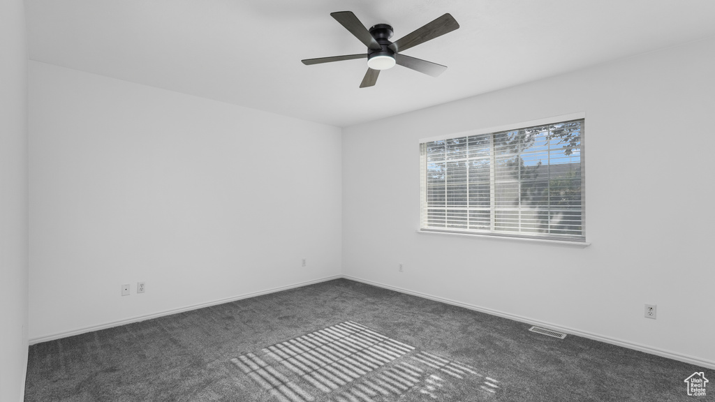 Spare room with dark colored carpet, a ceiling fan, and baseboards