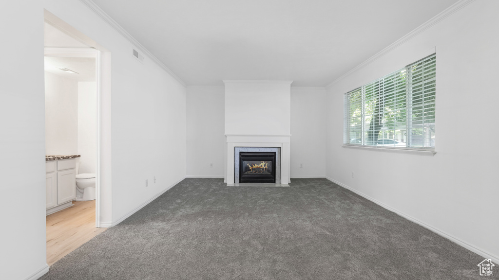 Unfurnished living room featuring a fireplace with flush hearth, carpet floors, ornamental molding, and baseboards