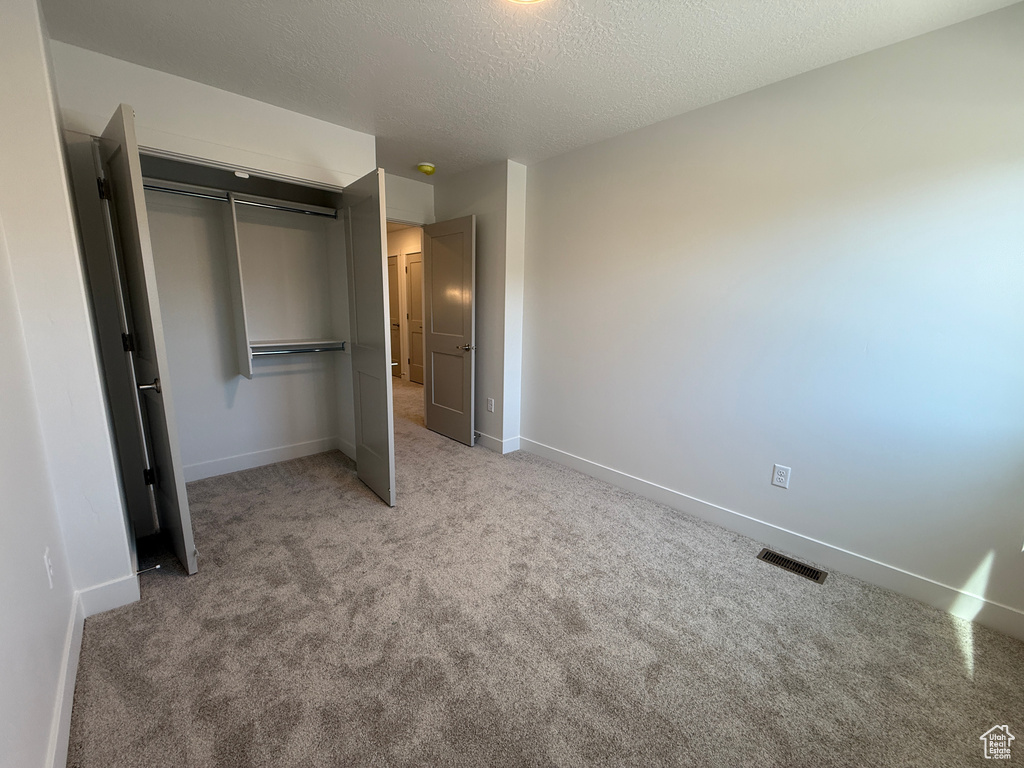 Unfurnished bedroom featuring a closet, carpet, baseboards, and a textured ceiling