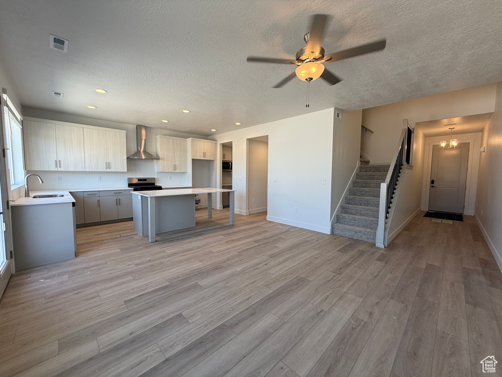 Kitchen with wall chimney exhaust hood, a sink, light wood-style flooring, a center island, and a textured ceiling