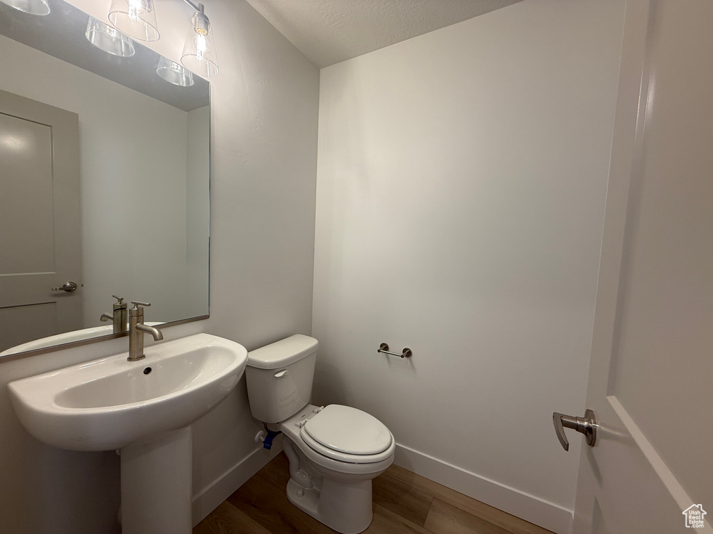Half bathroom with toilet, baseboards, wood finished floors, and a sink