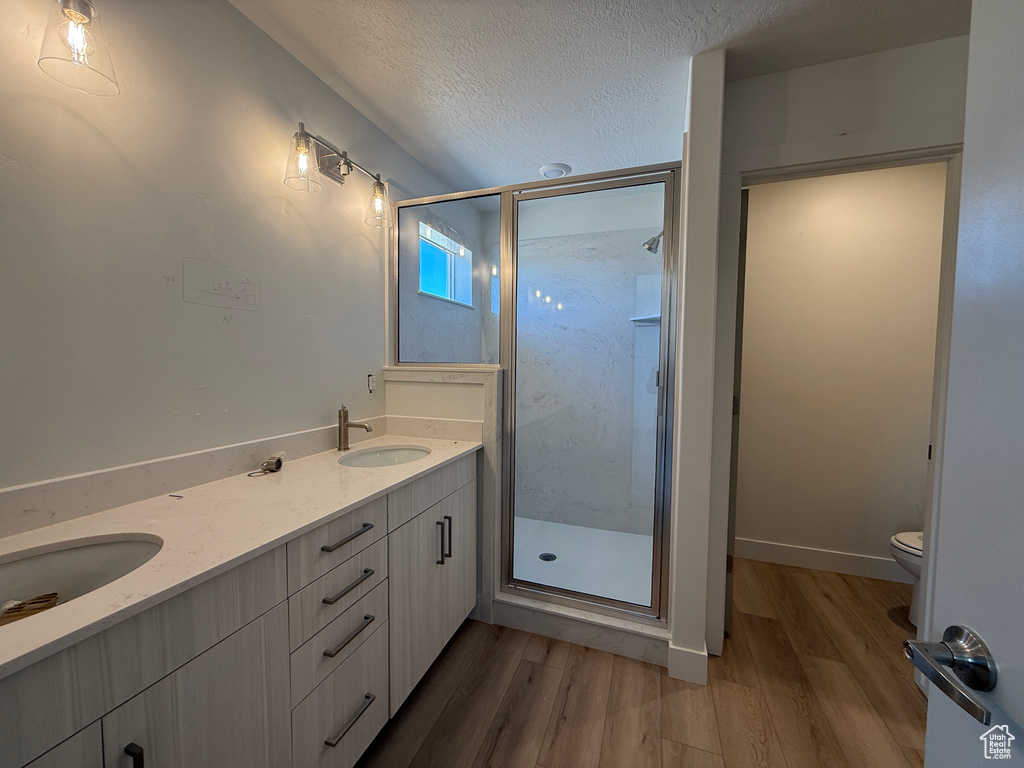 Full bath with wood finished floors, a shower stall, toilet, a textured ceiling, and double vanity