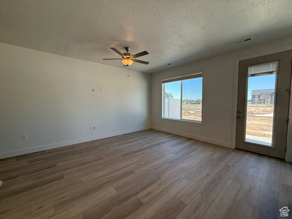 Empty room featuring a textured ceiling, wood finished floors, baseboards, and ceiling fan