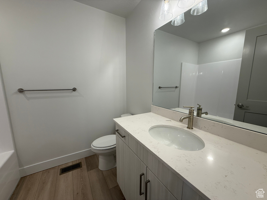 Full bathroom with wood finished floors, toilet, vanity, baseboards, and a shower