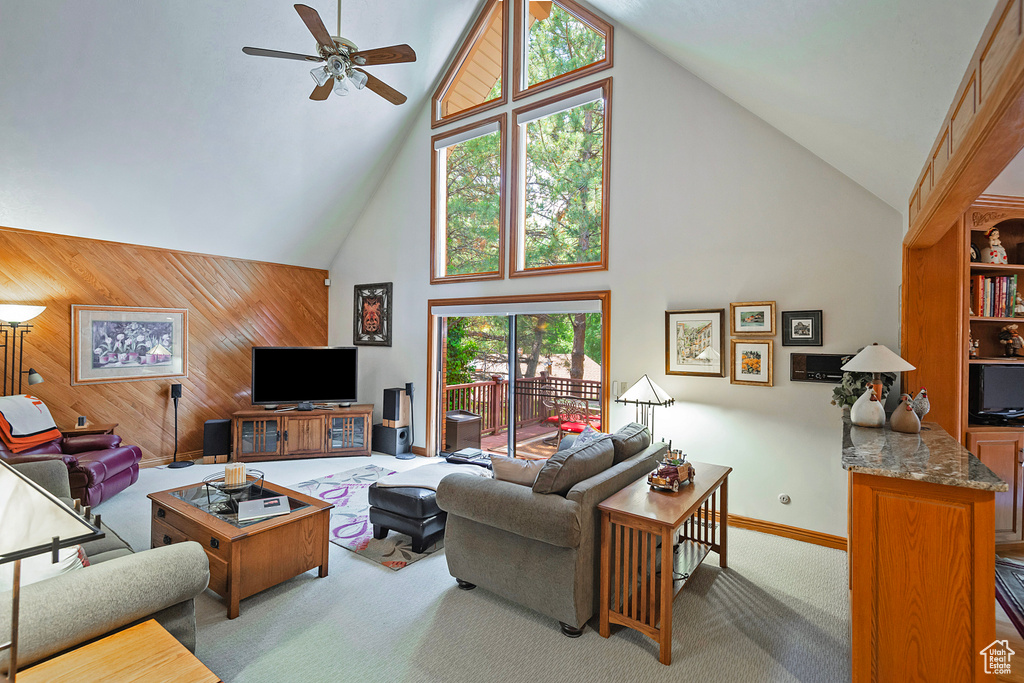 Living room with high vaulted ceiling, wood walls, ceiling fan, carpet flooring, and baseboards