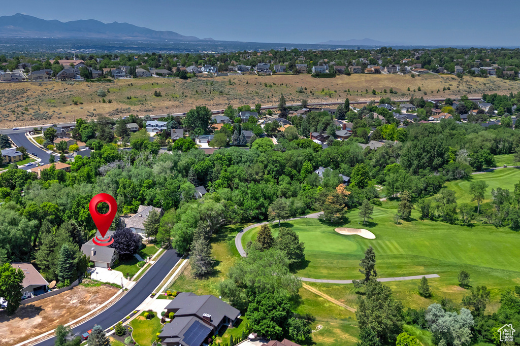 Aerial view of property and surrounding area featuring a mountainous background, a golf course, and nearby suburban area