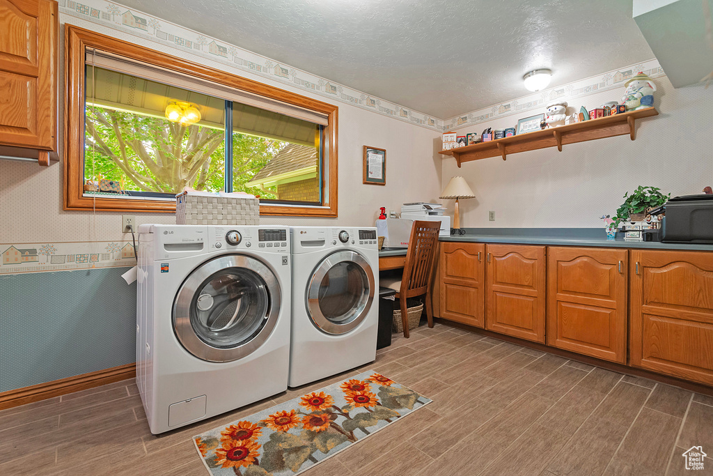 Washroom with cabinet space, wood finished floors, separate washer and dryer, a textured ceiling, and wallpapered walls