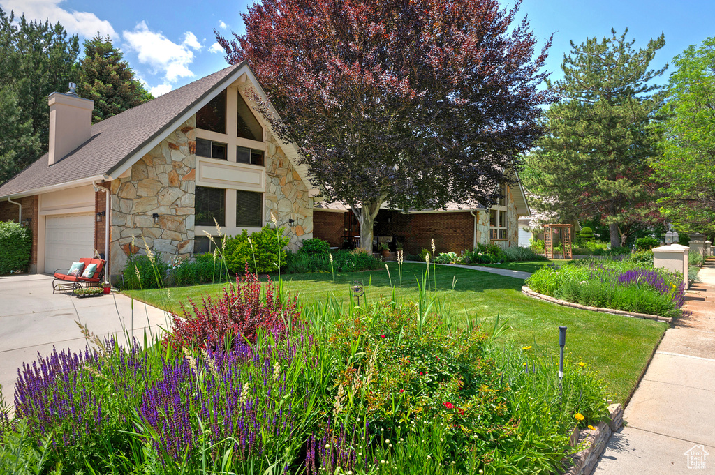 View of front of house featuring stone siding, a front yard, a chimney, an attached garage, and driveway