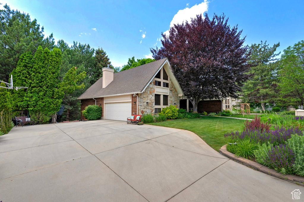View of front of house featuring stone siding, a front yard, an attached garage, concrete driveway, and a chimney