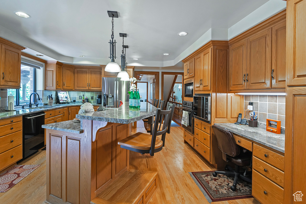 Kitchen with black appliances, a sink, light wood-type flooring, a center island, and backsplash