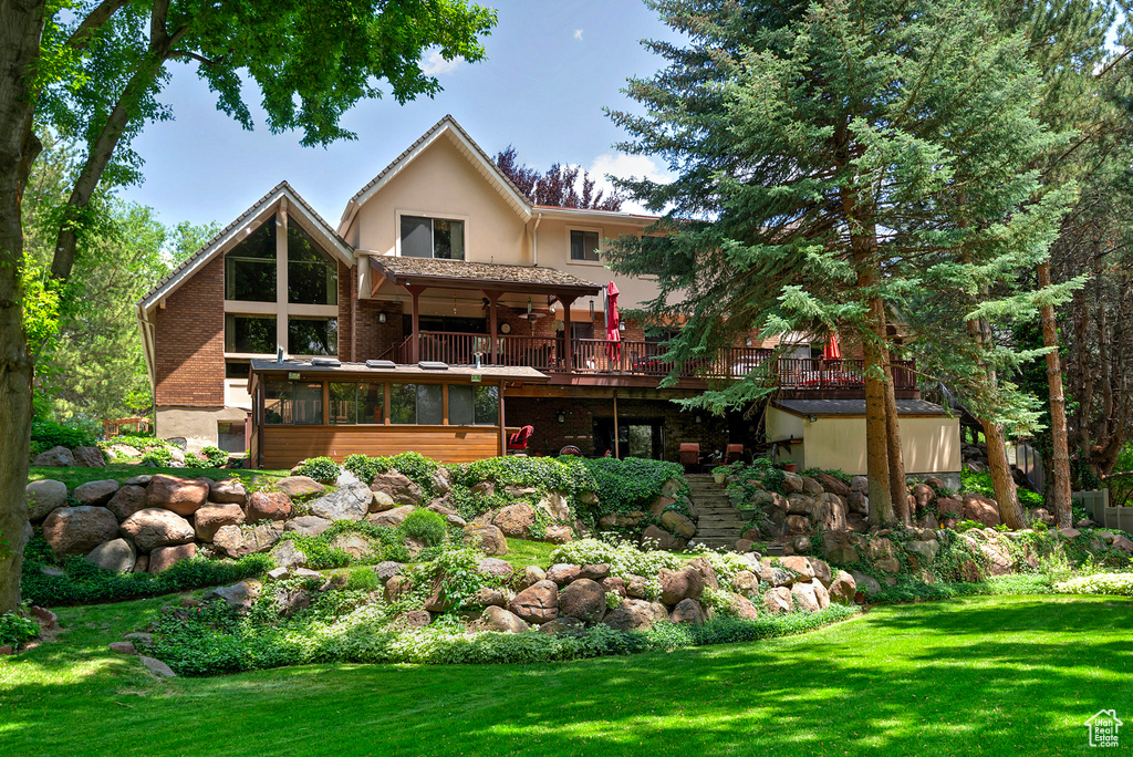 Rear view of house featuring a sunroom, a yard, a deck, and stucco siding