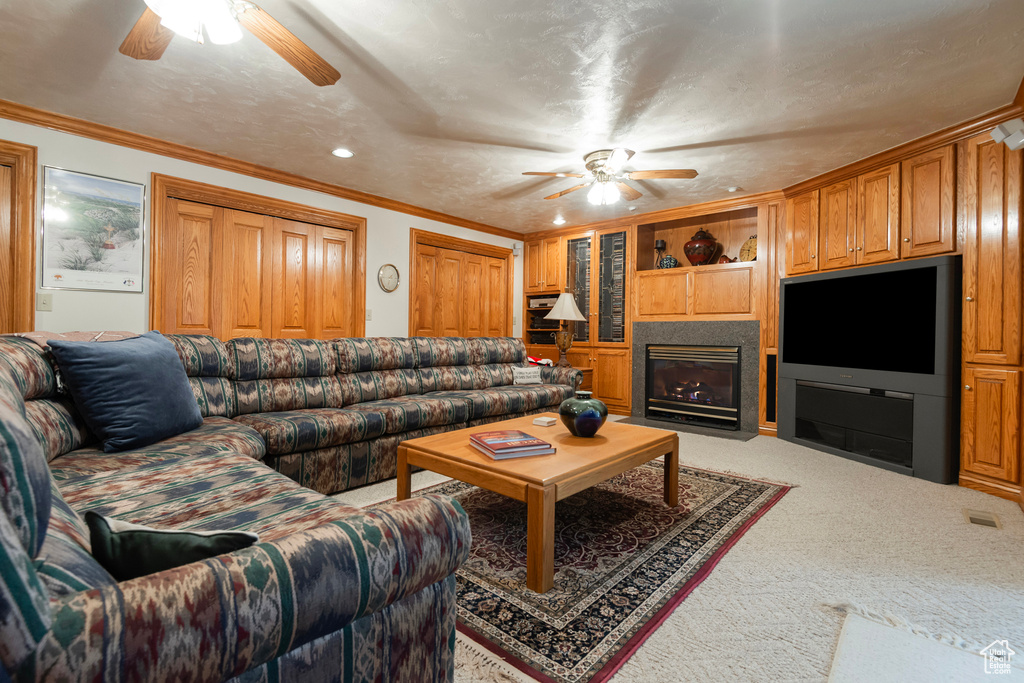 Living area featuring ceiling fan, light colored carpet, ornamental molding, a fireplace with flush hearth, and recessed lighting