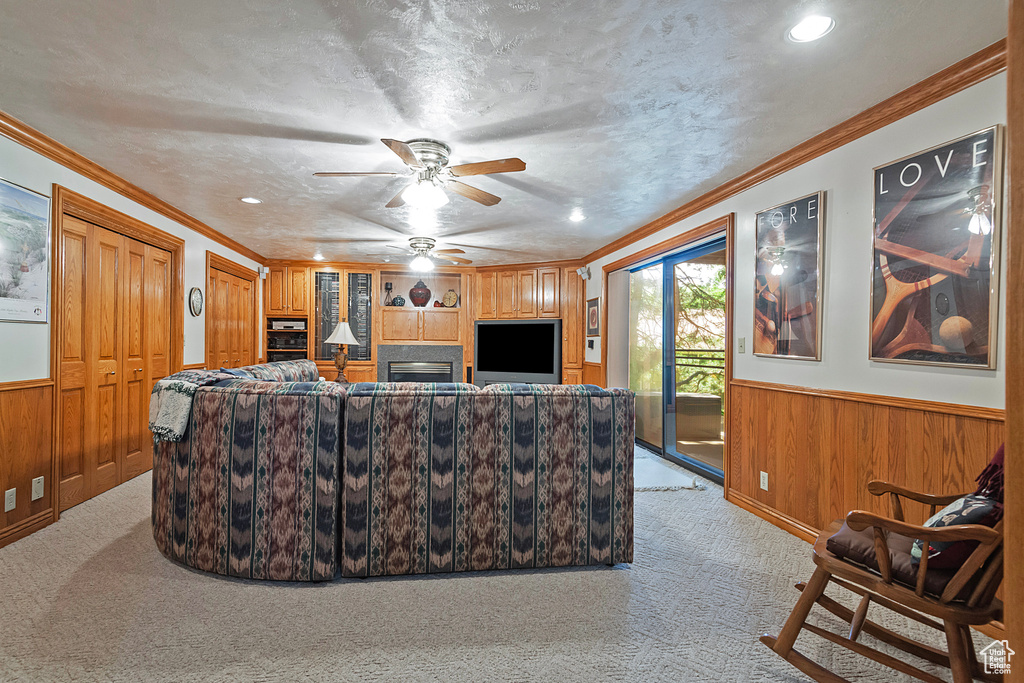 Living room with light colored carpet, wood walls, wainscoting, ceiling fan, and ornamental molding