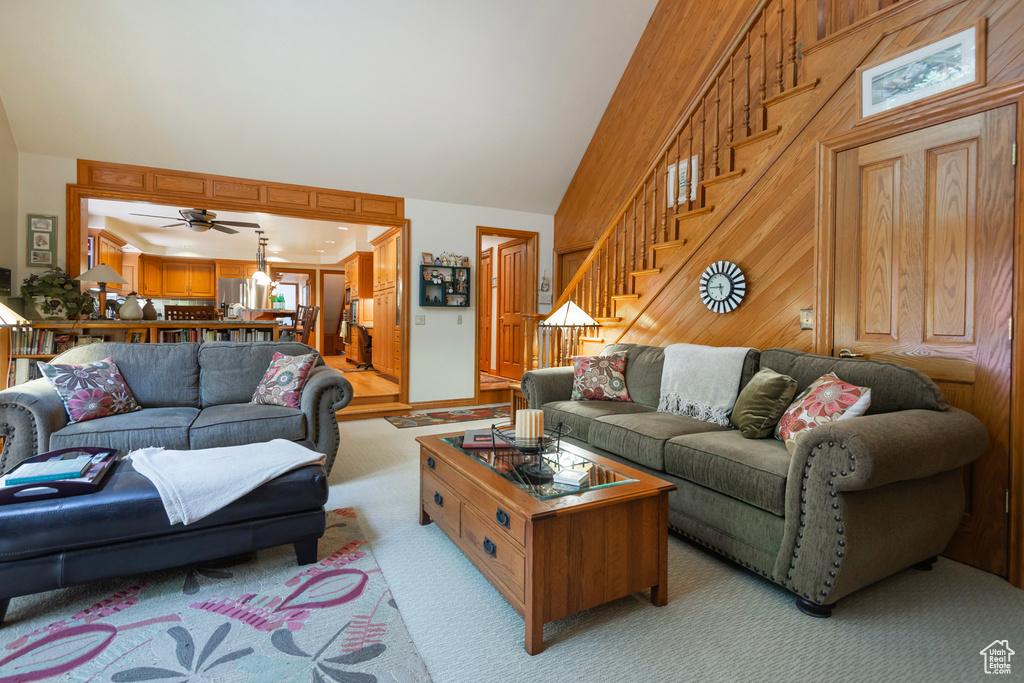 Living area with light colored carpet, stairs, a ceiling fan, and high vaulted ceiling