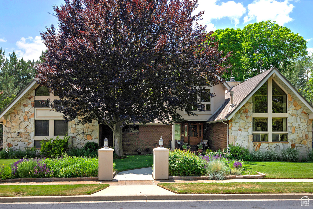 View of front of house with stone siding, a front yard, and a shingled roof