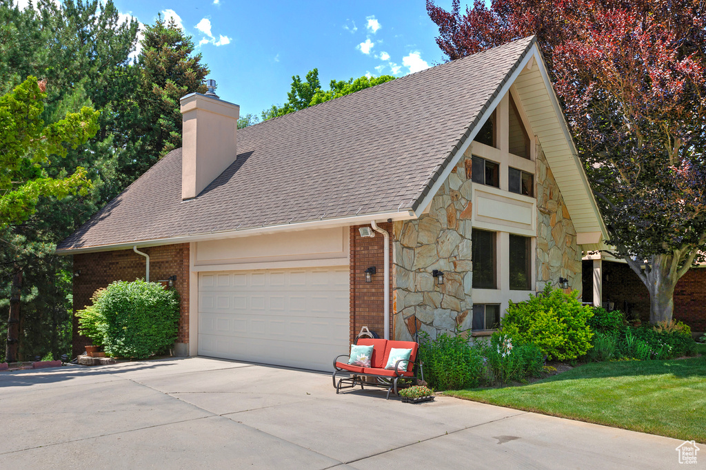 View of front of house featuring stone siding, a chimney, driveway, a garage, and a shingled roof