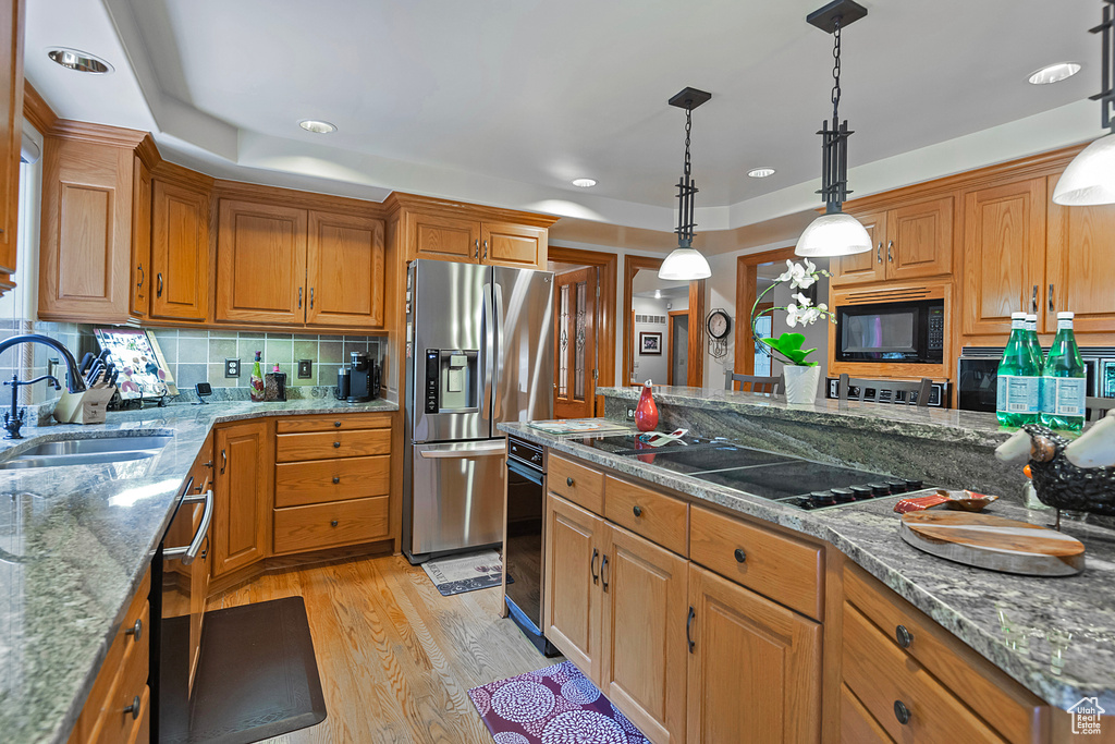 Kitchen featuring black appliances, a sink, light wood-style flooring, tasteful backsplash, and brown cabinets