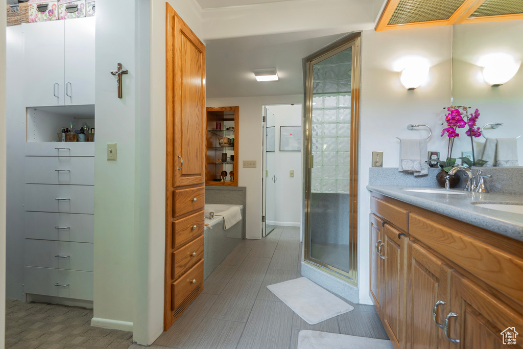 Full bathroom featuring a bath, double vanity, a shower stall, and baseboards
