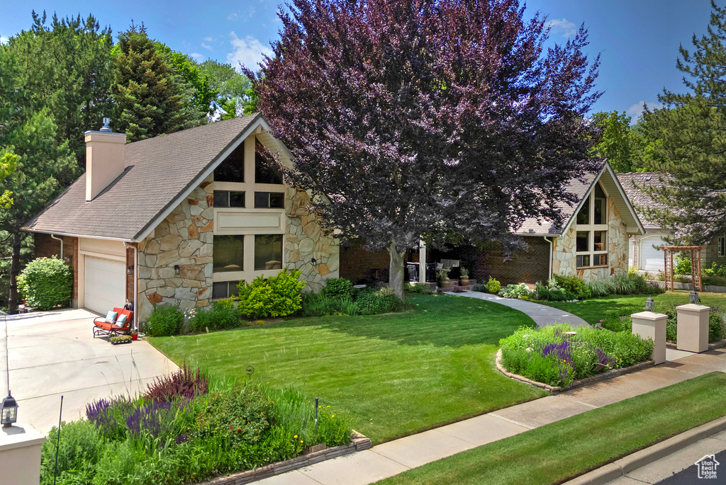 View of front of house with stone siding, a chimney, a front yard, a garage, and concrete driveway