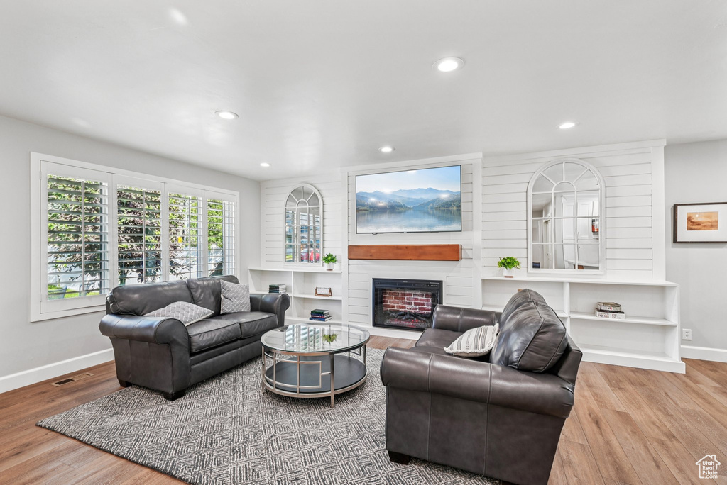 Living room featuring baseboards, wood finished floors, recessed lighting, and a large fireplace