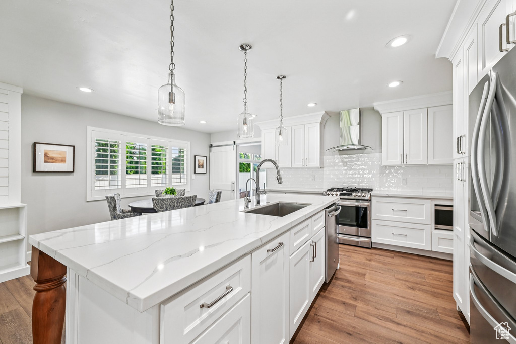 Kitchen featuring wall chimney range hood, a sink, stainless steel appliances, recessed lighting, and an island with sink