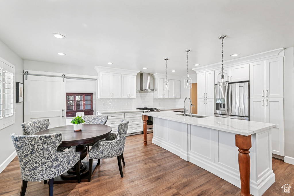 Kitchen with appliances with stainless steel finishes, a sink, wall chimney exhaust hood, recessed lighting, and a kitchen island with sink