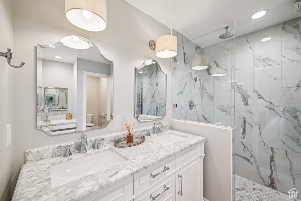 Bathroom with toilet, a marble finish shower, double vanity, and recessed lighting