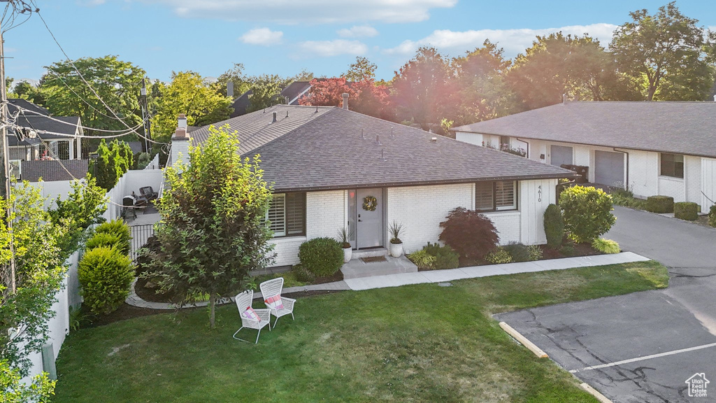 Ranch-style house featuring a shingled roof, a front lawn, brick siding, and a chimney
