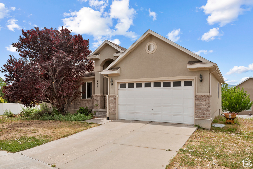 View of front of home with an attached garage, stucco siding, concrete driveway, and brick siding